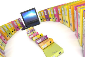 Image of a laptop computer surrounded by binders of files as an example of exemption certificate management.